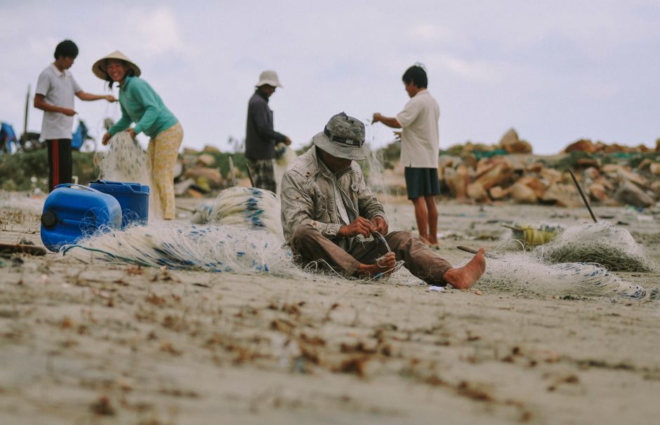 Local Albanian fishermen mending nets on shingle beach Ksamil
