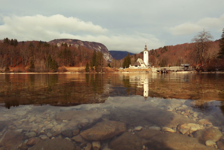 Bohinj Lake Slovenia beach pebbles blue water Triglav Peak background sunny day