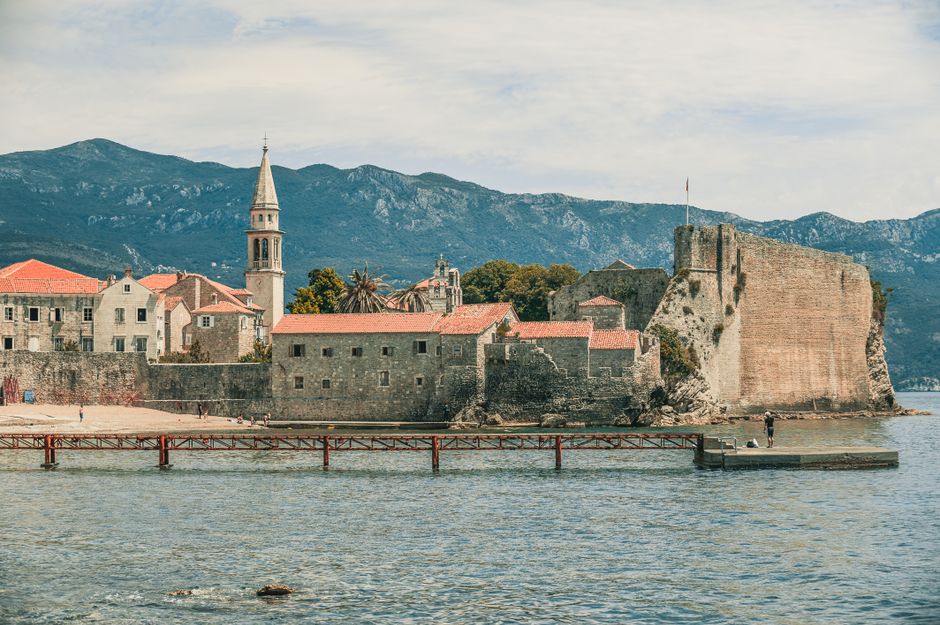 Kayaker paddling past Risan Fortress Montenegro stone walls mountain backdrop